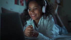 Laughing African young girl with headphones watching something on laptop at home