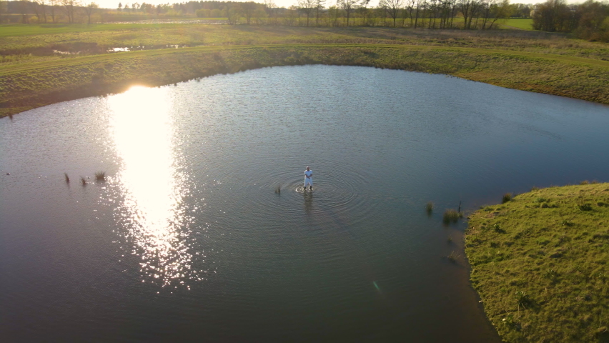Man Enjoys Dancing In A Pond In The Countryside Field During Sunrise. - Drone Orbit Shot