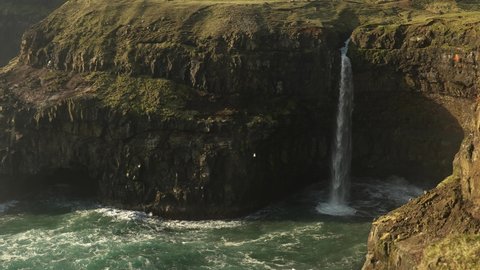 Slow motion shot of Múlafossur waterfall and crashing waves of Atlantic against coastline on Vagar Island,Faroe Island