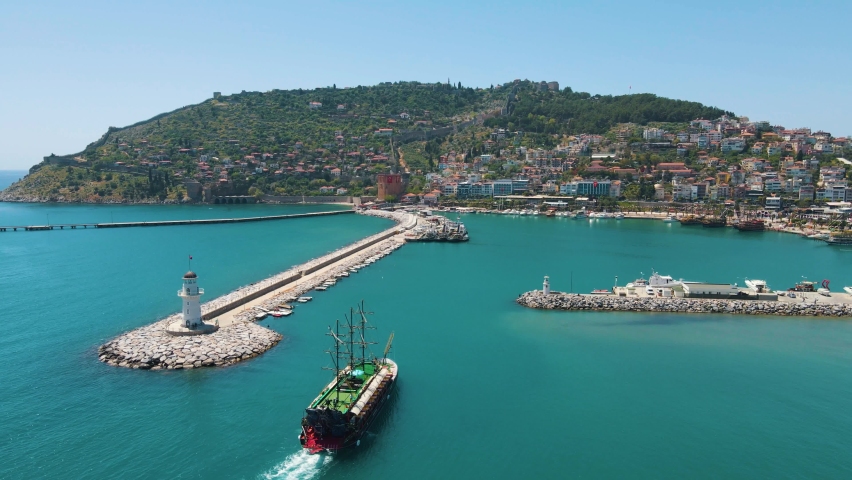 Excursion ship enters the marina of Alanya. Kizil Kule or Red Tower and port aerial panoramic view in Alanya city, Antalya Province on the southern coast of Turkey. White lighthouse at the port