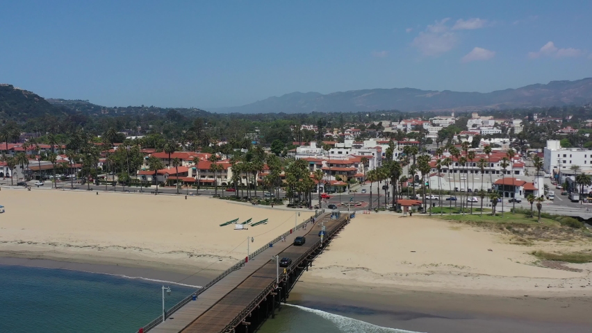 aerial drone of cars crossing the Stearns Wharf Pier in downtown Santa Barbara on a sunny summer day in California with large mountains in the distance Royalty-Free Stock Footage #1090298903