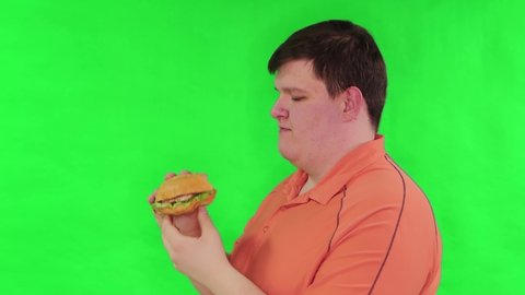 Portrait of a fat guy eating a big burger isolated on a green background. Chroma key, green screen. The concept of fast food and obesity.