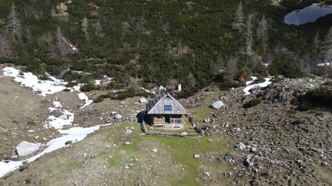 aerial shot, the camera moves away from the shepherd's hut, mountain hut and reveals the beautiful alpine surroundings of the pasture where patches of snow are visible in early spring