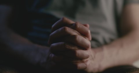 CLOSE UP of a young man bringing hands together to pray whilst breathing deeply and clasping hands together tightly. CINEMATIC, STATIC SHOT.
