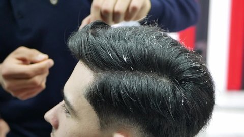 Stylish young guy sitting in a barber shop, close up. Barber making a fashionable haircut. Beauty salon Barber shop and haircut concept.
