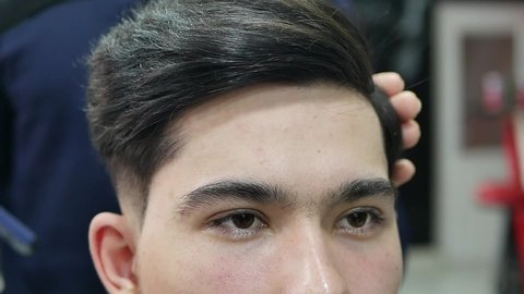 Stylish young guy sitting in a barber shop, close up. Barber making a fashionable haircut. Beauty salon Barber shop and haircut concept.