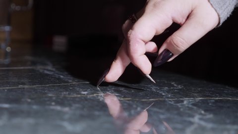 close-up, female fingers with long black nails step on a black reflective surface.