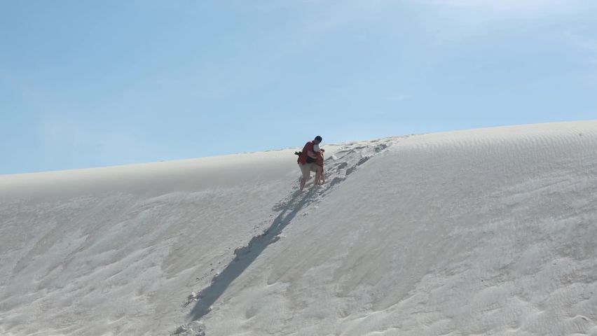 father helps his son up a sand dune in desert