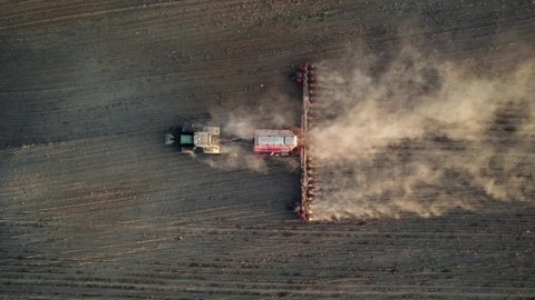 Top aerial view: Agricultural tractor with special trailed equipment works the land before sowing crops, raising the dust into the air. Concept of cultivated field, Agronomy farming husbandry. High