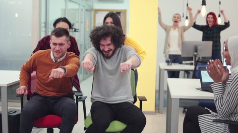 Group of young coworkers enjoying chair race at work, slow motion
