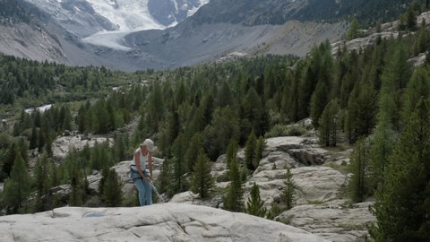Drone view of female mountain climber rappelling on rock face. Aerial view of sporty woman rock climbing in summer in an alpine climate in the Swiss Alps, glacier on the background.