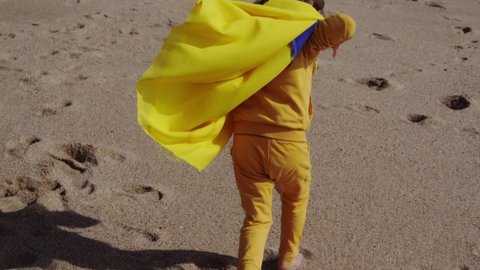 Little Girl with flag of Ukraine running on the sandy beach by the sea. Stop war between Russia and Ukraine, power of Ukraine, patriotism