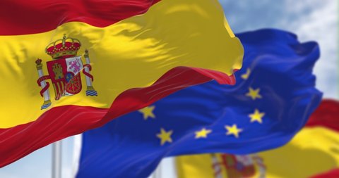 Seamless slow motion loop of the national flag of Spain waving in the wind with blurred european union flag in the background on a clear day. Democracy and politics. European country. Selective focus.