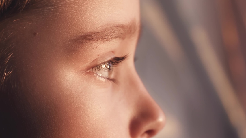 Close-up of the child's eyes. The child's face. The boy looks out the window, his face is illuminated by the rays of the sun. Royalty-Free Stock Footage #1090316075