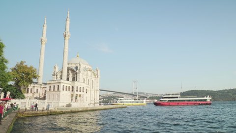 Istanbul, Turkey - September 16, 2021: Ferry is mooring on the shore in Istanbul, Turkey. View of Ortakoy Mosque and the Bosphorus Bridge (the 15 July Martyrs Bridge) connecting Europe to Asia.