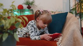 Portrait of worried funny little teen child girl enthusiastically playing racing video online games on mobile phone. School toddler kid using smartphone gadget app with shooter simulator at home alone