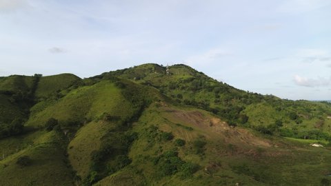 A green mountain with steep slopes covered with forest trees and meadow grass. Mountain landscape of wild nature of Dominican Republic. Sunny summer day on the sea coast.