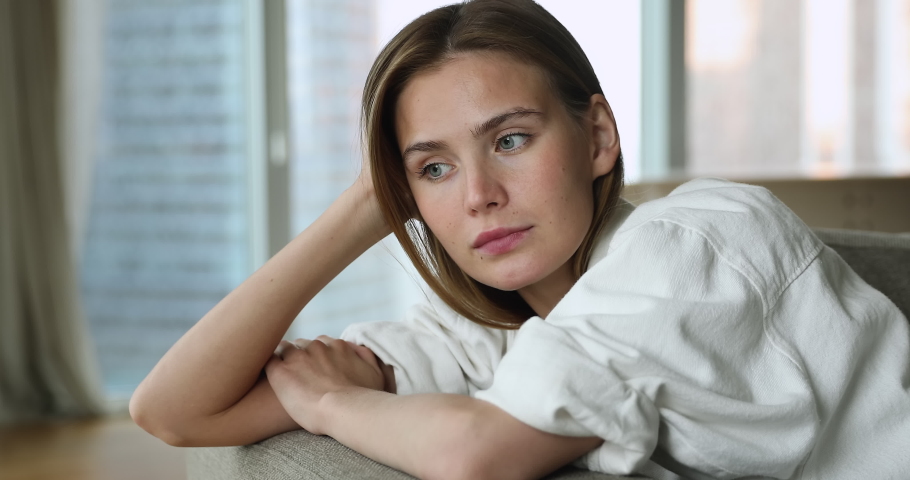 Close up beautiful sad blond young 25s woman reflecting seated on sofa, bored at home alone, relaxing looks thoughtful deep in thoughts, waiting or missing her boyfriend, thinks, recollects concept Royalty-Free Stock Footage #1090320081