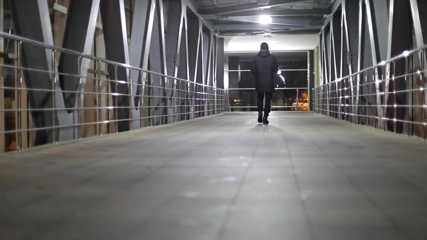 Bridge across road. Pedestrian area. Light in tunnel. Man walks inside tunnel.