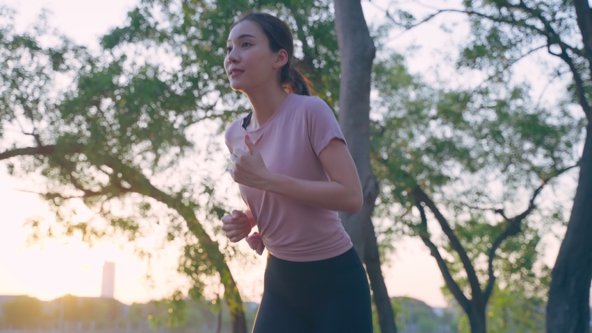 Asian young beautiful sport woman running on street in public park. Beautiful athlete fit and firm girl in sportswear exercise by jogging workout outdoor for health care in evening sunset in garden. Royalty-Free Stock Footage #1090324557