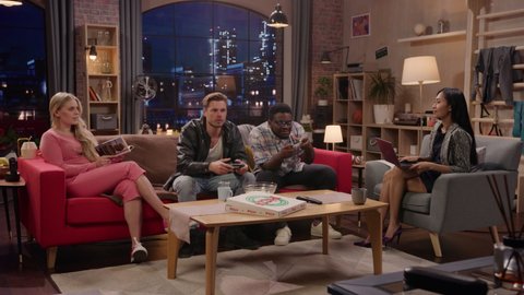 Television Sitcom: Four Diverse Friends having Fun in the Living Room. Funny TV Show Girls Reading and Working, Guys Playing Video Games on a Sofa. Comedy Series on Playback Channel, Streaming Service