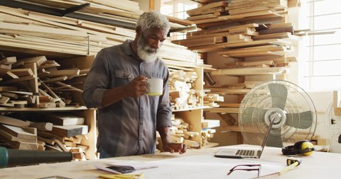 African american male carpenter drinking coffee in a carpentry shop. carpentry, craftsmanship and handwork concept
