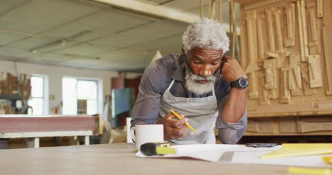 Thoughtful african american male carpenter sketching a project in a carpentry shop. carpentry, craftsmanship and handwork concept