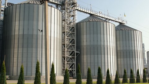 Large modern plant for storage and processing of grain crops. View of granary on sunny day. Big iron barrels of grain. Silver silos on agro manufacturing plant for processing and drying.
