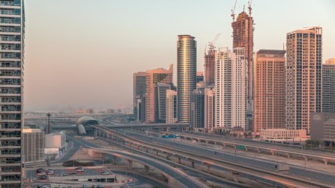 Dubai Marina with long shadows on skyscrapers and Sheikh Zayed road with metro railway aerial timelapse during sunrise. Traffic on a highway near modern towers, United Arab Emirates