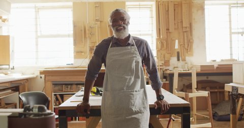 Portrait of african american male carpenter wearing an apron standing in a carpentry shop. carpentry, craftsmanship and handwork concept