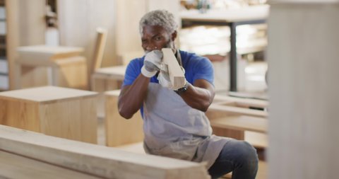 African american male carpenter looking and choosing wooden plank in a carpentry shop. carpentry, craftsmanship and handwork concept