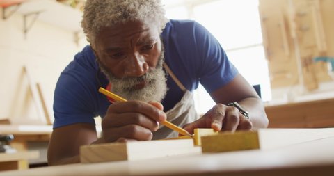 African american male carpenter making pencil markings on wooden plank. carpentry, craftsmanship and handwork concept