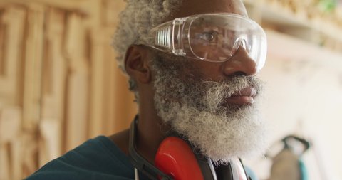 Close up view of african american male carpenter wearing safety glasses in a carpentry shop. carpentry, craftsmanship and handwork concept