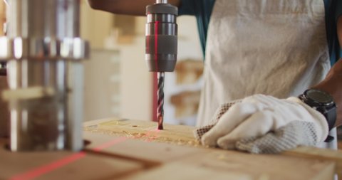 Mid section of african american male carpenter drilling wood with a laser drill in a carpentry shop. carpentry, craftsmanship and handwork concept