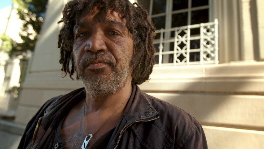 Homeless person portrait. Closeup of a senior man with dreadlocks and gray beard looking at camera while standing outside. | Shutterstock HD Video #1090330927