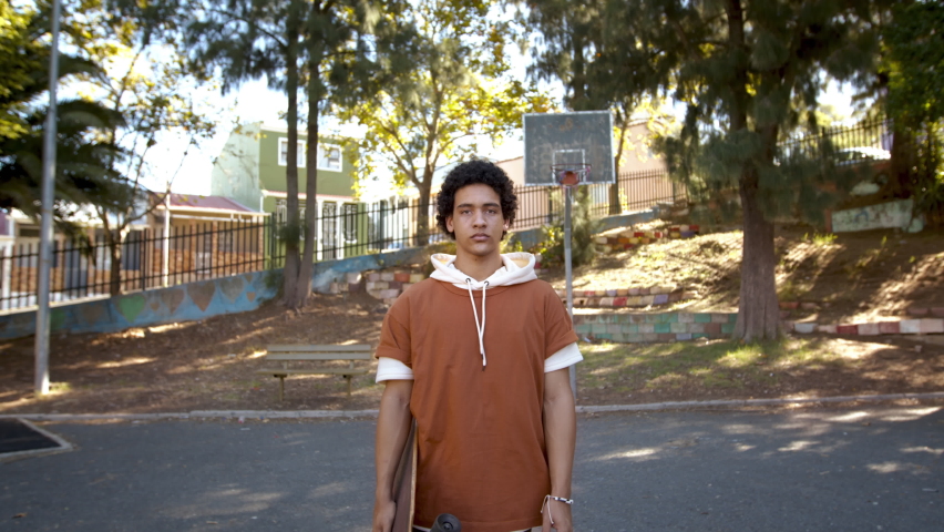 Portrait of a teenage boy holding a skateboard standing outside. Teen skater looking at camera with blank expression. | Shutterstock HD Video #1090330931