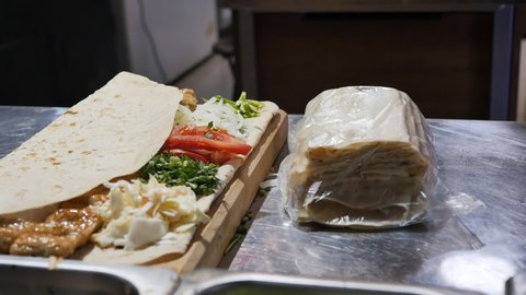 the hands of the cook serve the client a kebab with chopped fresh vegetables and herbs on a thin bread pita bread and a wooden board. Ready Armenian kebab