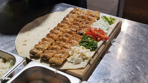 the hand of the cook holding a silicone brush smears the hot kebab with melted butter. The butter is melted from the hot lula kebab.
