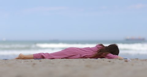 kid girl is doing stretching exercises, changes pose to snake on mat on beach by the sea. child practicing yoga on the beach.