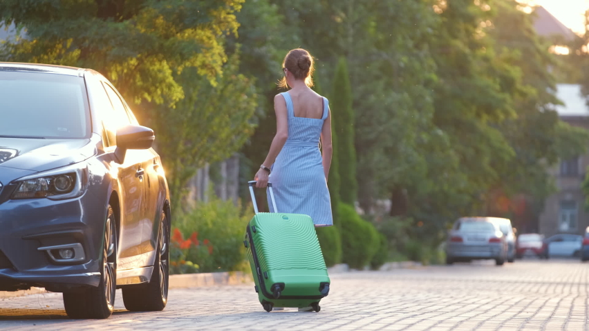 Young woman driver taking green suitcase out from her car walking down the street. Travelling and vacations concept | Shutterstock HD Video #1090332911