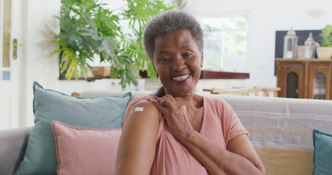 African american senior woman showing the band aid on her shoulder sitting on the couch at home. medical healthcare concept