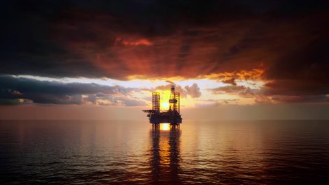 Moving over the ocean waves at sunset towards the silhouette of an offshore oil and gas production platform.