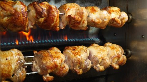 Roasted chickens rotating on spit on barbecue grill, delicious grilled chicken