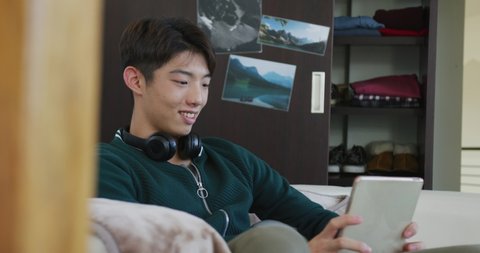 Asian boy using digital tablet sitting on the couch at home. teenager lifestyle and living concept
