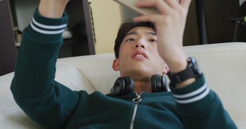 Asian boy playing games on digital tablet lying on the couch at home. teenager lifestyle and living concept