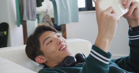Asian boy playing games on digital tablet lying on the couch at home. teenager lifestyle and living concept