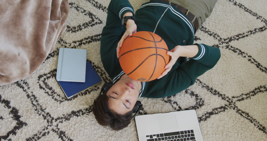 Overhead view of asian boy playing with basketball lying on the floor at home. teenager lifestyle and living concept
