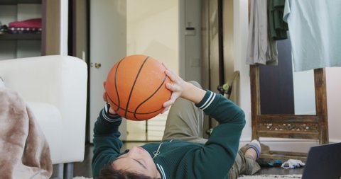 Asian boy playing with basketball lying on the floor at home. teenager lifestyle and living concept