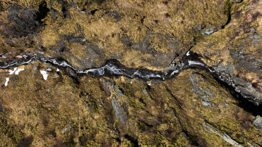 Drone tracking river flowing down rugged rocky Italian alp mountain hillside
