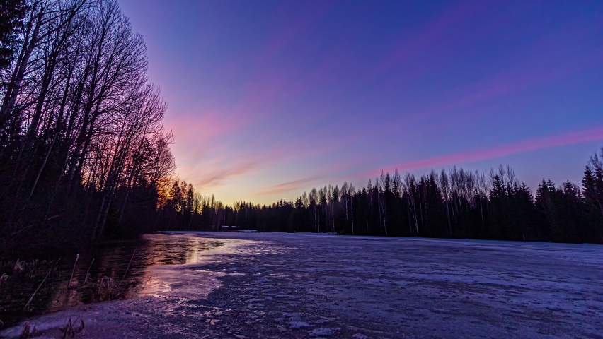 Close up shot over snow melting of lake surrounded by forest on all sides with sun movement in timelapse throughout the day in rural countryside.